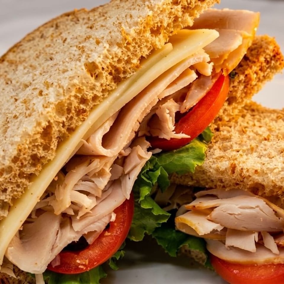 Two halves of a turkey and cheese sandwich on whole wheat bread with lettuce and tomato.